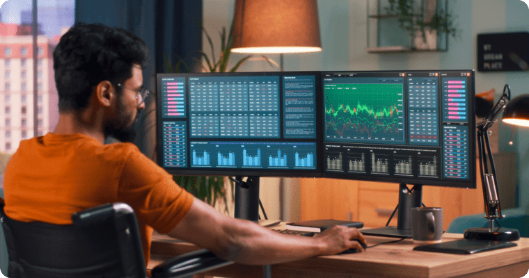 Photo d’un homme regardant des graphiques sur trois écran d’ordinateur dans son bureau 