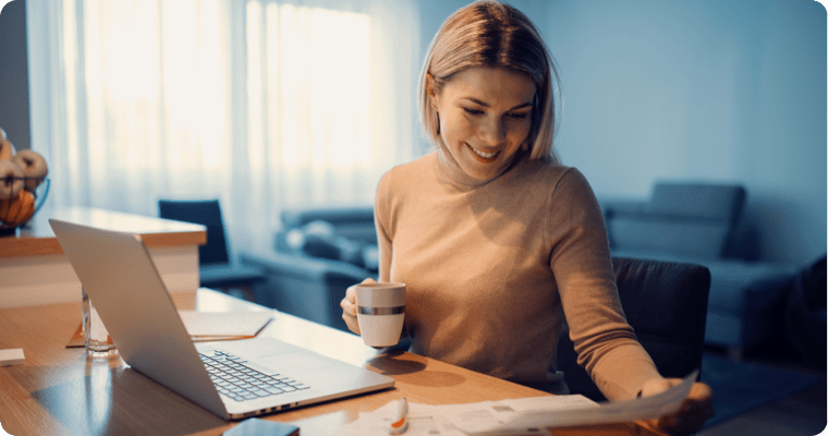 Photo d’une femme qui consulte des documents en prenant son café dans son salon