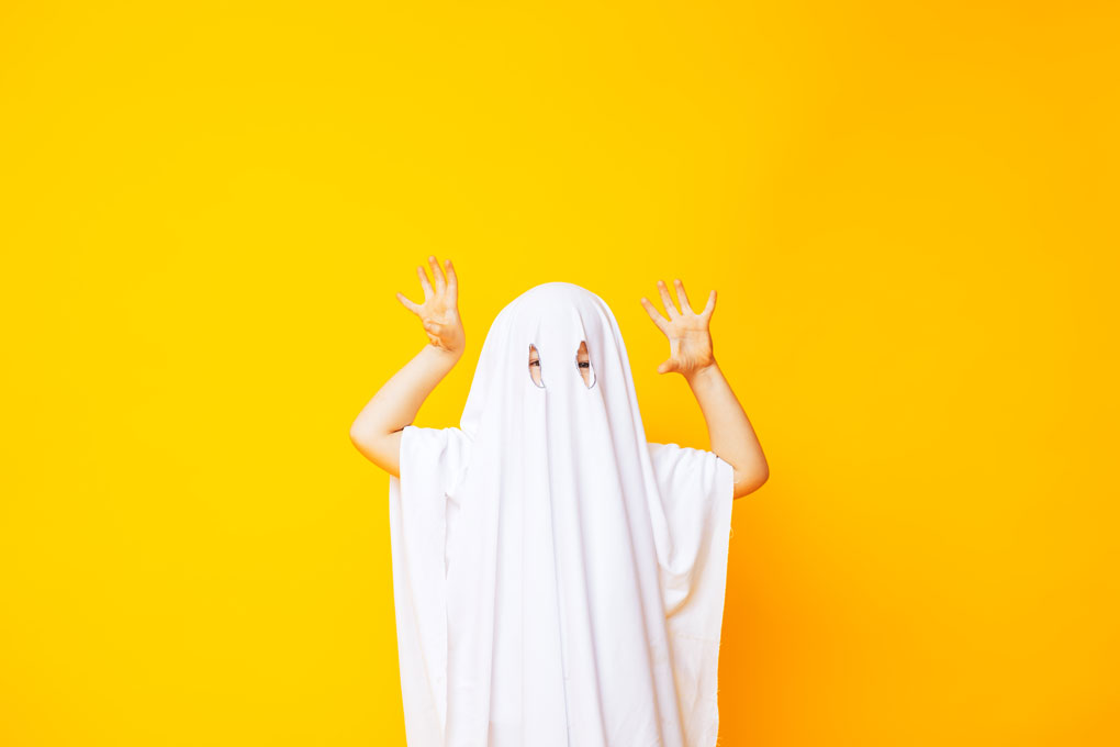 Un enfant déguisé en fantôme qui tente de faire peur avec ses mains
