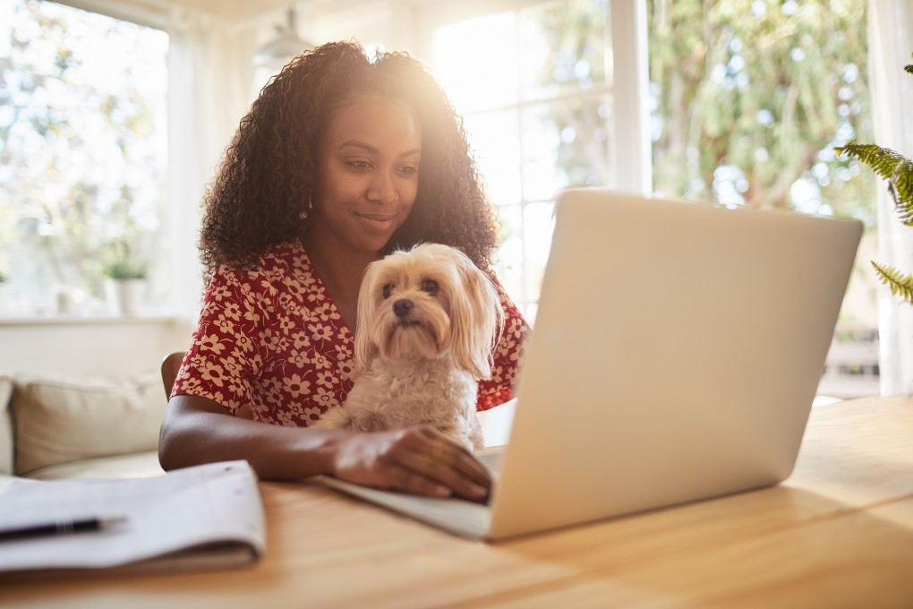 Femme qui sourit devant son ordinateur avec son chien sur les genoux
