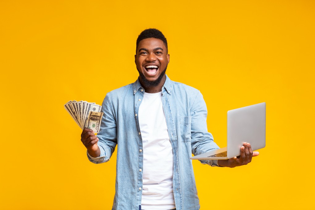 Homme souriant qui tient de l’argent et son ordinateur